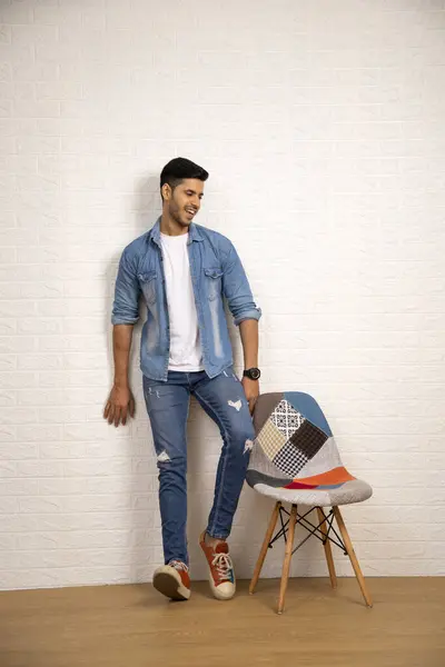 Hintli erkek model duvarın yanında duruyor ve arkasına yaslanıyor.