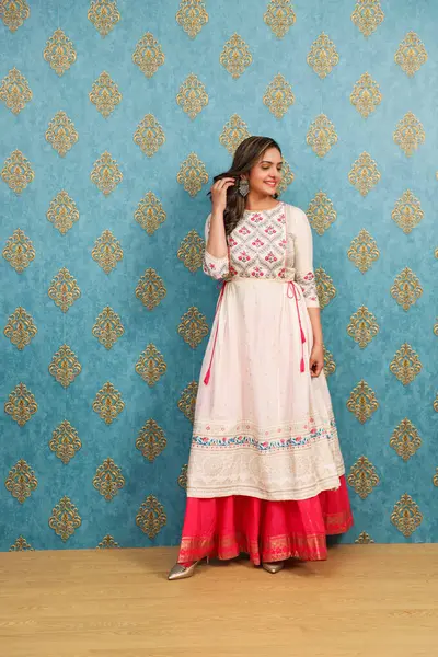 Geleneksel giyinmiş çekici bir kadın duvarın önünde dikilirken poz veriyor.