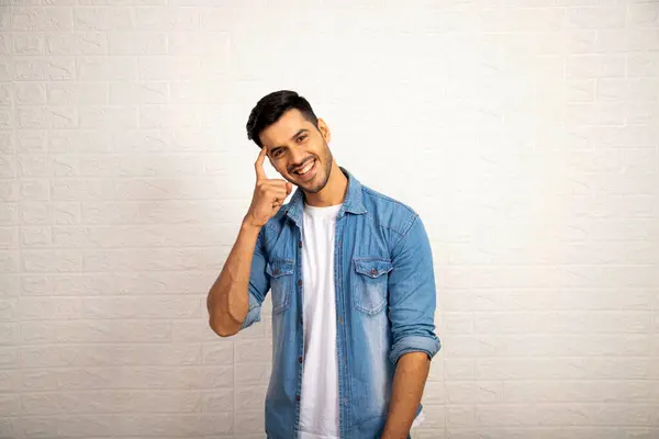 Beyaz arka planda dikilirken kafasında parmak olan yakışıklı bir adam.