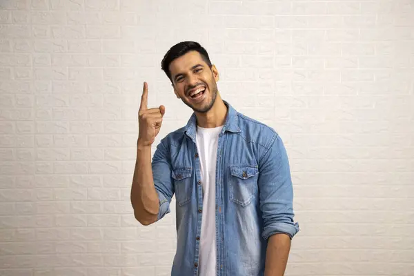 Kot gömlekli çekici adam gülümsüyor ve işaret parmağını kameranın önünde yukarı kaldırıyor.