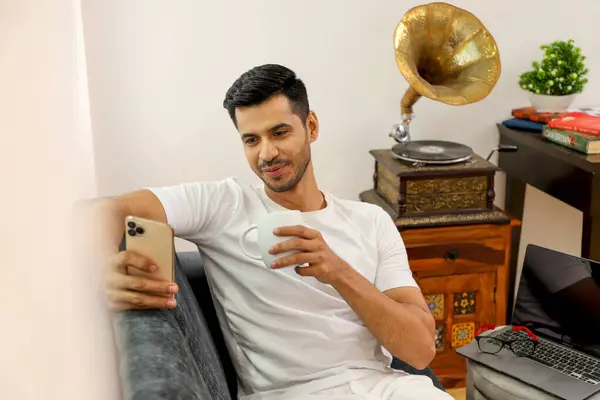 Genç adam kanepede otururken internetten video izlemek için telefon kullanıyor.