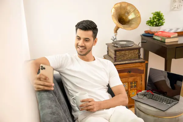 Gülümseyen adam film izlemekten ve gramofonun yanındaki koltukta oturup kahve içmekten zevk alıyor.