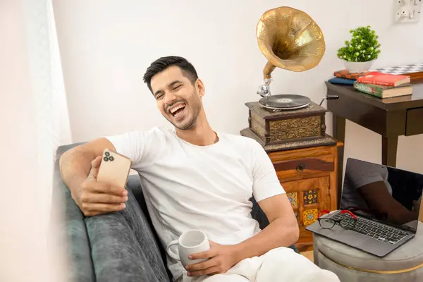 Mutlu Adam 'ın resmi, beyaz giysi, günlük kıyafet, koltukta oturmak, oturma odası, beyaz bardak, cep telefonu, gülümseme.