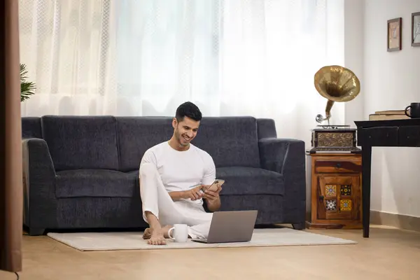 Çalışan adam dizüstü bilgisayarla çalışırken cep telefonuna mesaj yazıyor.