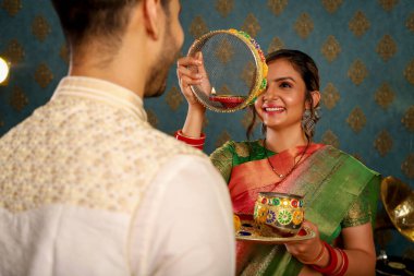 Karwa Chauth festivalini geleneksel kıyafetlerle kutlayan genç bir çiftin fotoğrafı.