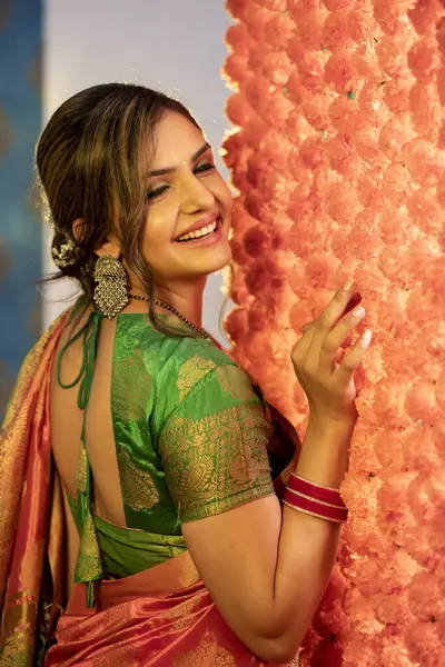 一个穿着传统服装的年轻貌美的女人站在装饰着花朵的墙边笑着的照片 图库图片