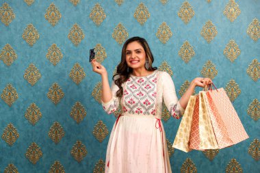 Diwali kutlaması sırasında takım elbiseli bir kadın alışveriş çantalarını tutuyor ve bankamatik kartını kameraya doğrultuyor.