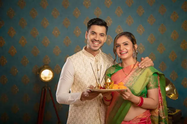 Olgun bir Hintli çift kameraya poz verirken puja tabağı taşıyor ve geleneksel kıyafetlerle Diwali 'yi kutluyor.