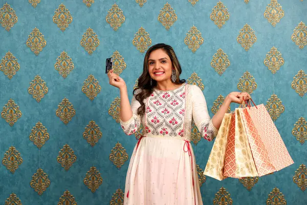一名身着西服的妇女在庆祝Diwali时拿着购物袋 指着相机方向的借记卡 免版税图库图片