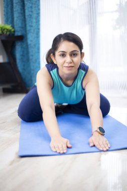 Evde yoga minderinde oturan kadın yoga pozu veriyor.