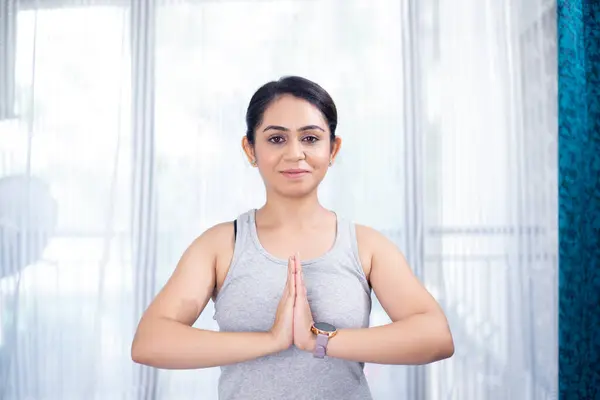 namaste yogası giymiş sportif bir kadın. Evinin camının önünde duruyor.