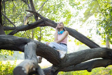 Alone Woman talking on phone while sitting on tree branch