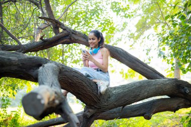 A smiley teenage girl using her phone while sitting in a park