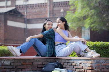 Attractive womans are sitting and staring at each other in the university park.