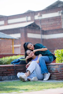 One bright student pulling her friend cheeks on the college campus