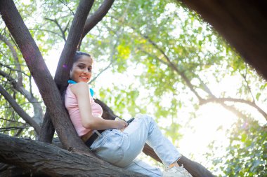 Cute beautiful woman with a headset around her neck, smiling and lying on a tree branch