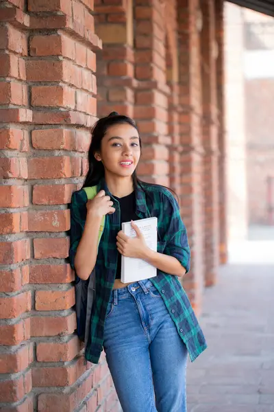 A appealing woman standing on a college campus with books in her hand