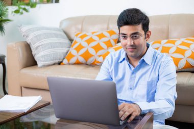 Evde çalışırken dizüstü bilgisayarda çalışan mavi gömlekli genç bir profesyonel. 