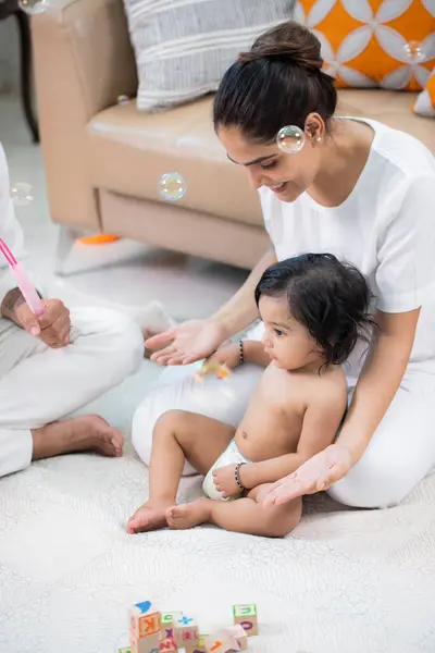 Annesiyle oturan tatlı erkek bebek sabun köpüğüyle oynuyor.