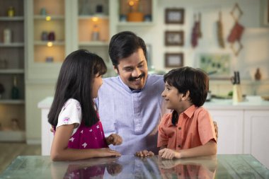 Baba evde otururken çocuklarıyla konuşuyor.