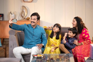 Çocuklu neşeli ebeveynler telefonda selfie çekerken gülüyorlar.