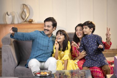 Baba, anne, kız ve oğul kamerada birlikte poz veriyorlar.