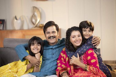 Nükleer Aile geleneksel kıyafetleriyle evde kameraya bakarken gülümsüyor.