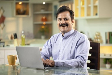 Kurta giymiş yetişkin adam kameraya bakarken sırıtıyor. 