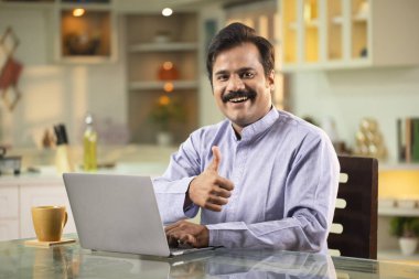 Dizüstü bilgisayarın önünde otururken Başparmağını gösteren adam