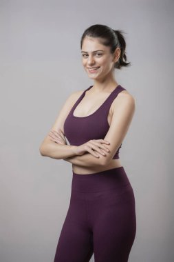 Bir fitness modeli gülümsüyor, kollarını kavuşturup kameraya bakıyor.