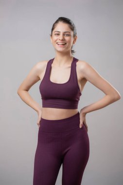 Yogacı kadın iki elini de beline koyup başka yere bakıyor.