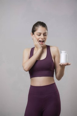 Mor spor elbiseli güzel bir manken elinde bir hap şişesi tutarken yüzündeki ifade.