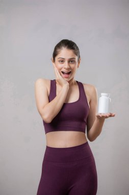 Güzel bir mankenin bir elinde tablet şişesi ve yüzünde heyecanlı bir ifade vardır. Bir elini yüzüne koydu.