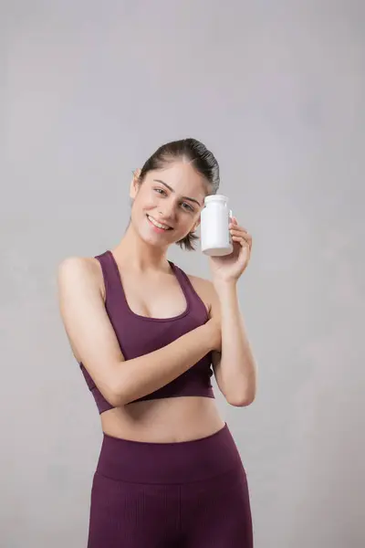 Spor elbiseli zeki bir kadın, tablet şişesini tutarken kafasını yana eğiyor.