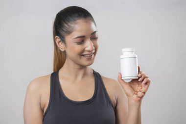 Spor kıyafeti giyen, elinde beyaz bir tablet şişeyle ona bakan sevimli bir kadının yakın plan fotoğrafı.