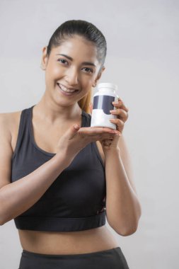 Yetişkin bir kadın elinde bir şişe hap tutarken kameranın önünde poz veriyor.