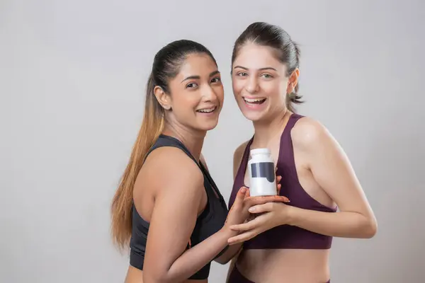 En seksi mankenlerden ikisi elinde ilaç şişesiyle kameraya bakıp gülümsüyor.