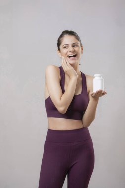 Gülümseyen manken bir şişe takviye ve vitamin tutuyor ve başka tarafa bakıyor.