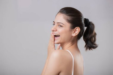 Yetişkin bir model gülümsüyor ve elini ağzını kapatarak poz veriyor.