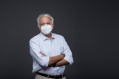 Siyah arka planda koruyucu maskeli olgun bir adamın portresi.