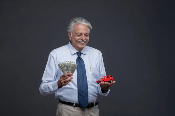 Zeki yaşlı bir adam bir elinde kırmızı bir fal oyuncağı, ona bakıyor ve diğer elinde Hint rupisi var.