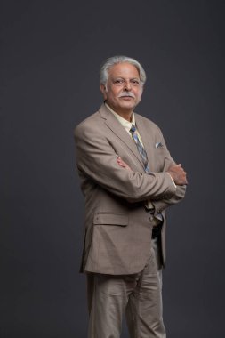 Takım elbiseli ve kravatlı kıdemli yönetmen kameranın önünde kollarını kavuşturarak poz veriyor.