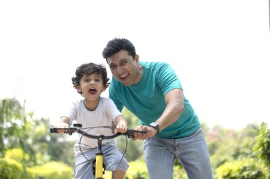 Akıllı çocuk babasının yardımıyla parkta bisiklet sürmeyi öğreniyor.