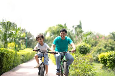 Parkta babasıyla bisiklete binen hoş çocuk.