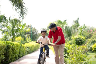 Küçük şampiyon parkta büyükbabasından bisiklet sürmeyi öğreniyor.
