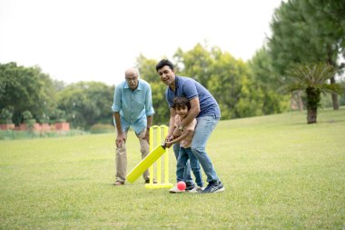 Baba ve oğlu büyükbabasıyla kriket oynuyorlar.