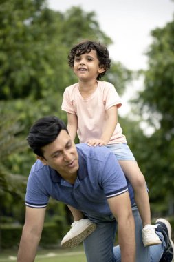 Yakışıklı baba, oğlunu sırtında parka götürüyor.