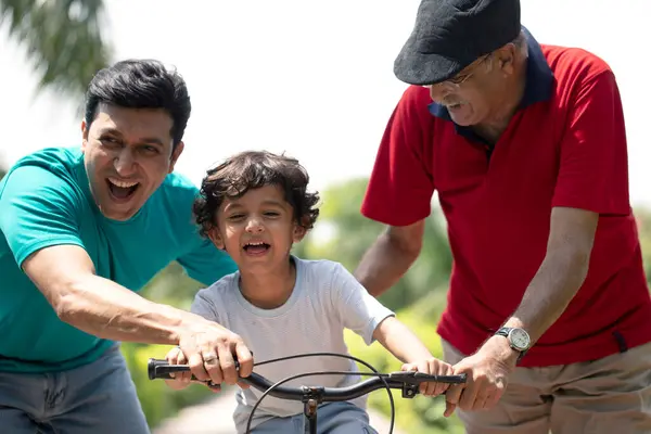 Masum çocuk parkta babasından ve büyükbabasından bisiklet öğreniyor.