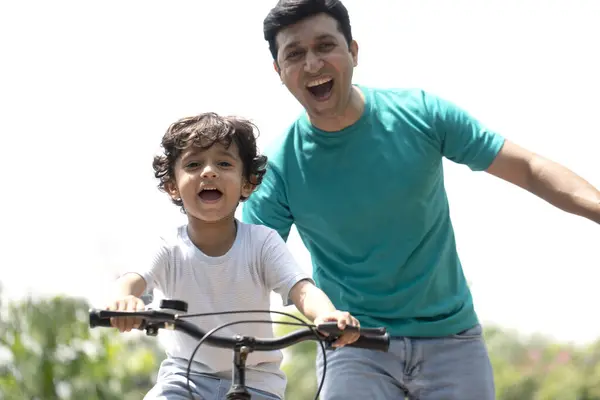 Babasının yardımıyla parkta bisiklet sürmeyi öğrenen hoş bir çocuk.
