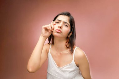 Beyaz elbiseli üzgün, güzel bir kadın pembe arka planda duruyor ve üzgün bir ifade sergiliyor.